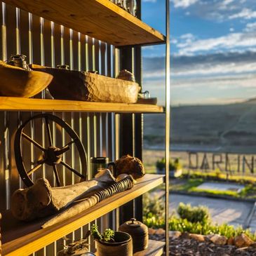 Sunlit rustic shelves with wooden and metal decor overlooking a scenic landscape.