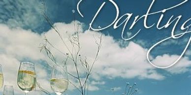 Wine glasses on a wooden table in a wildflower meadow under a blue sky.
