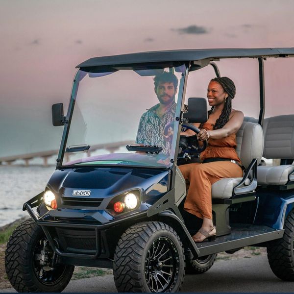 Happy couple driving golf cart on the beach in a beautiful sunset 