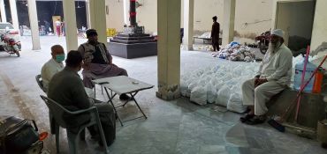 Four men sitting and talking indoors near packaged goods.