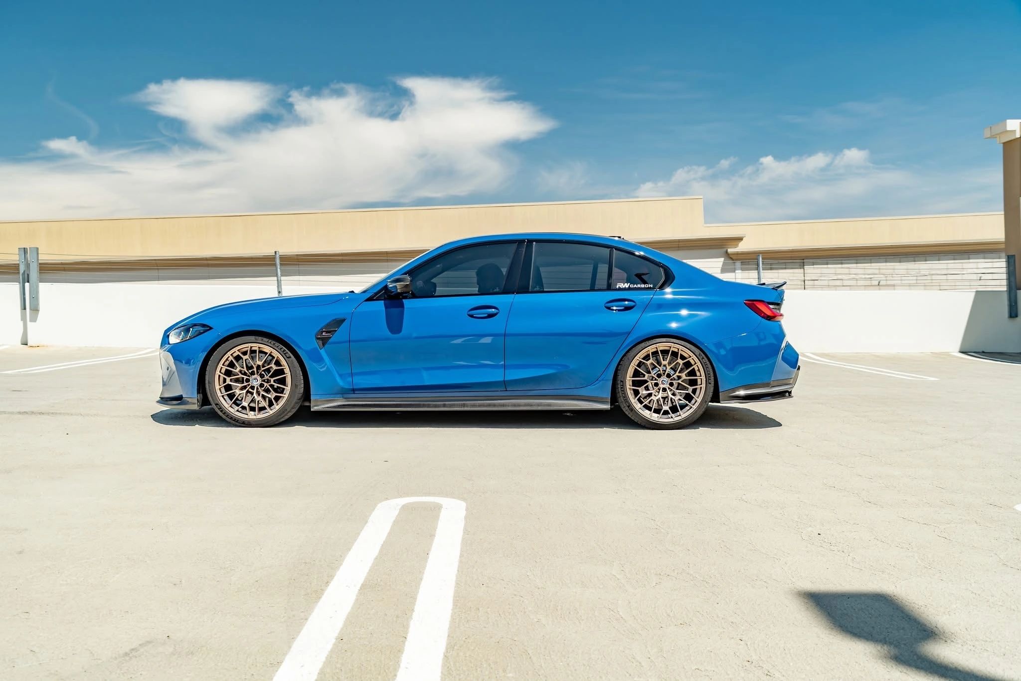 Blue BMW M3 with bronze wheels on a rooftop parking lot.