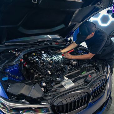 Technician working on a blue BMW engine at Bimmer Goats.