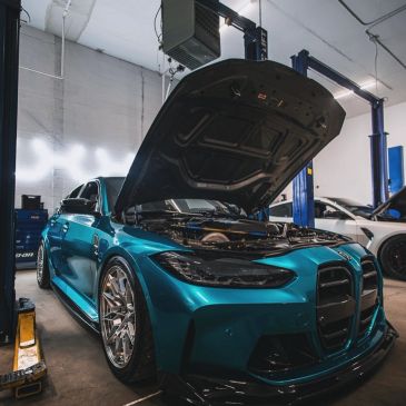 Turquoise BMW M3 with the hood open inside the Bimmer Goats workshop.