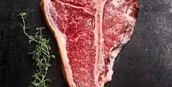 Raw T-bone steak with fresh herbs and olive oil on black surface.