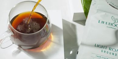 Lifeboost Coffee cup of coffee being poured into a clear glass mug