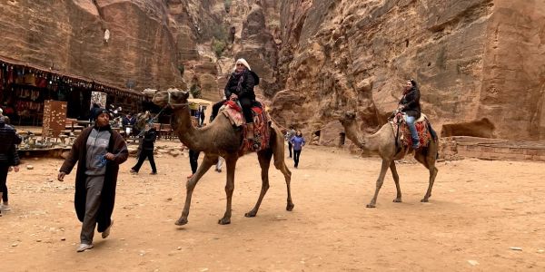People riding camels through a rocky canyon.