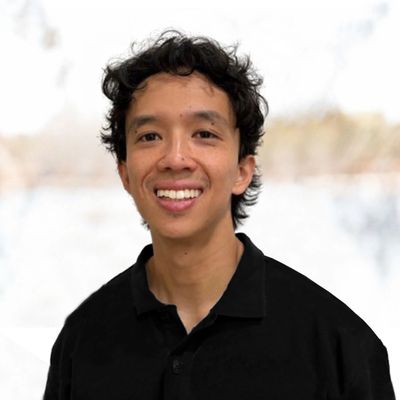 Young man with curly black hair smiling, wearing a black shirt.
