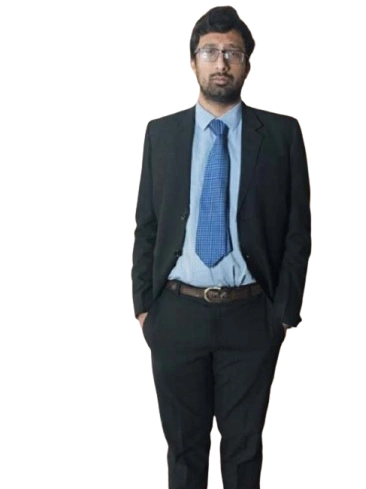Man in a black suit and blue tie standing with hands in pockets.
