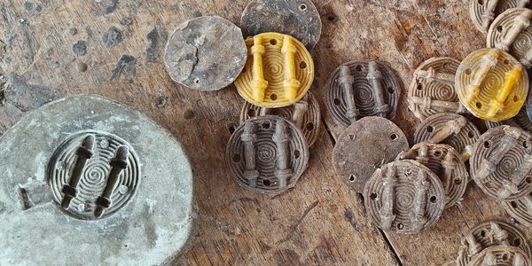 Wax discs with a design on them, next to a clay mould that has been used to make the design.