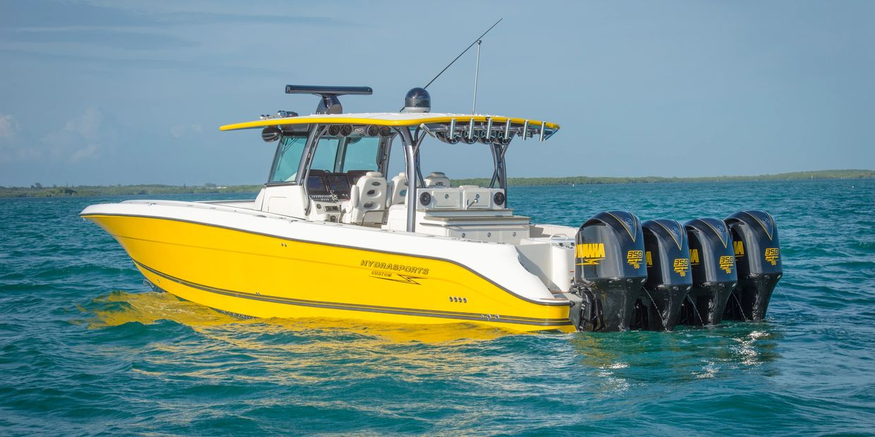 Yellow Hydrasports boat with a roof, and four motor engines at the back of the boat in the water.