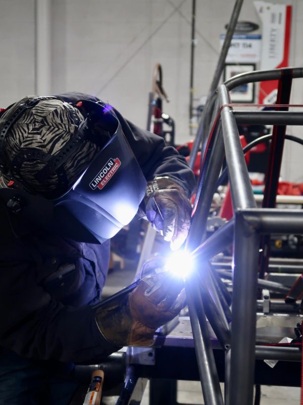 Welder working on metal frame with protective gear.