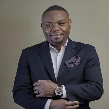 Man in a dark blazer with a watch, smiling confidently.
