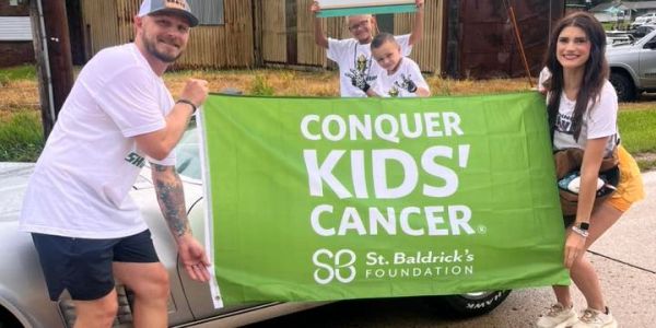 Group holding a banner promoting kids' cancer awareness by St. Baldrick's Foundation.