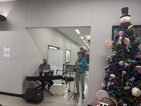Two musicians perform near a decorated Christmas tree indoors.