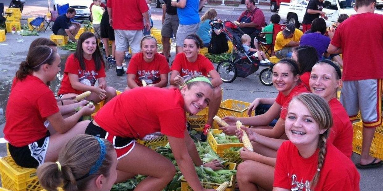 Group of kids husking corn together outdoors.