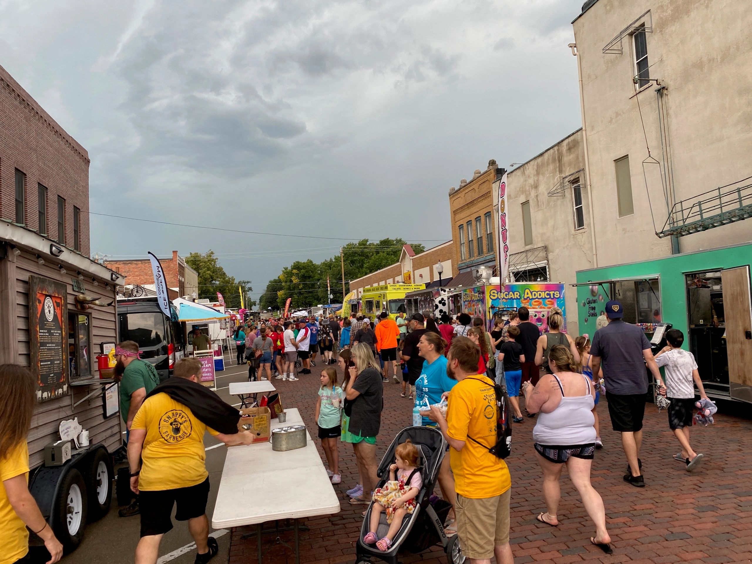 Crowded street festival with food trucks and people enjoying the event.