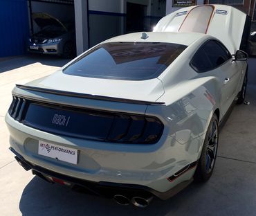 Rear view of a white Ford Mustang Mach 1 with open hood in a garage.