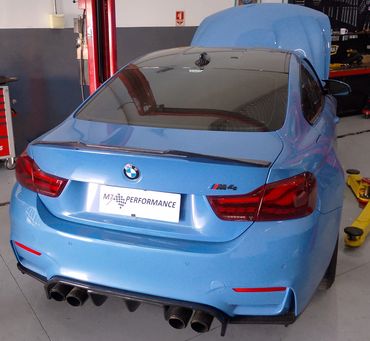 Rear view of a blue BMW M4 in a garage setting.