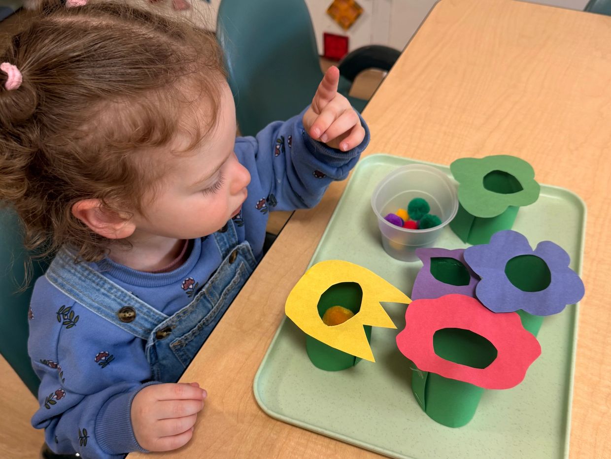 A child playing with colorful paper flowers and pom-poms at a table.