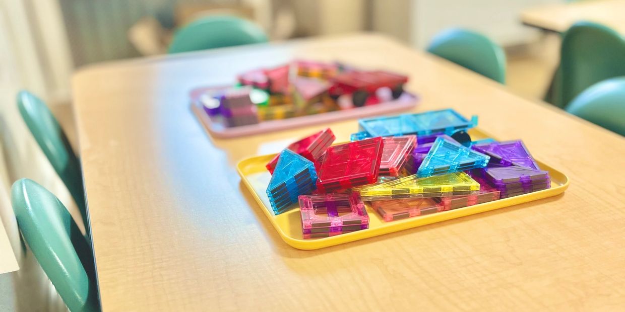 Colorful magnetic building tiles on trays on a classroom table.
