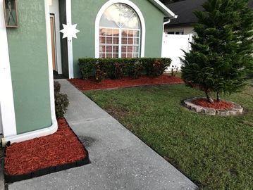 Neatly landscaped front yard with green grass and red mulch beds.