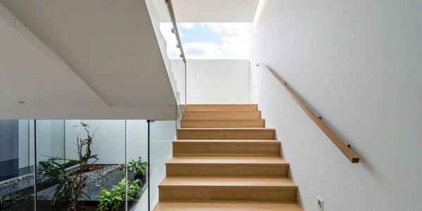 Modern wooden staircase with glass railing and natural light.