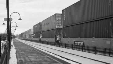 A freight train with stacked shipping containers passing a deserted platform.