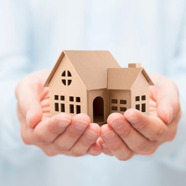 Hands holding a small cardboard model of a house.