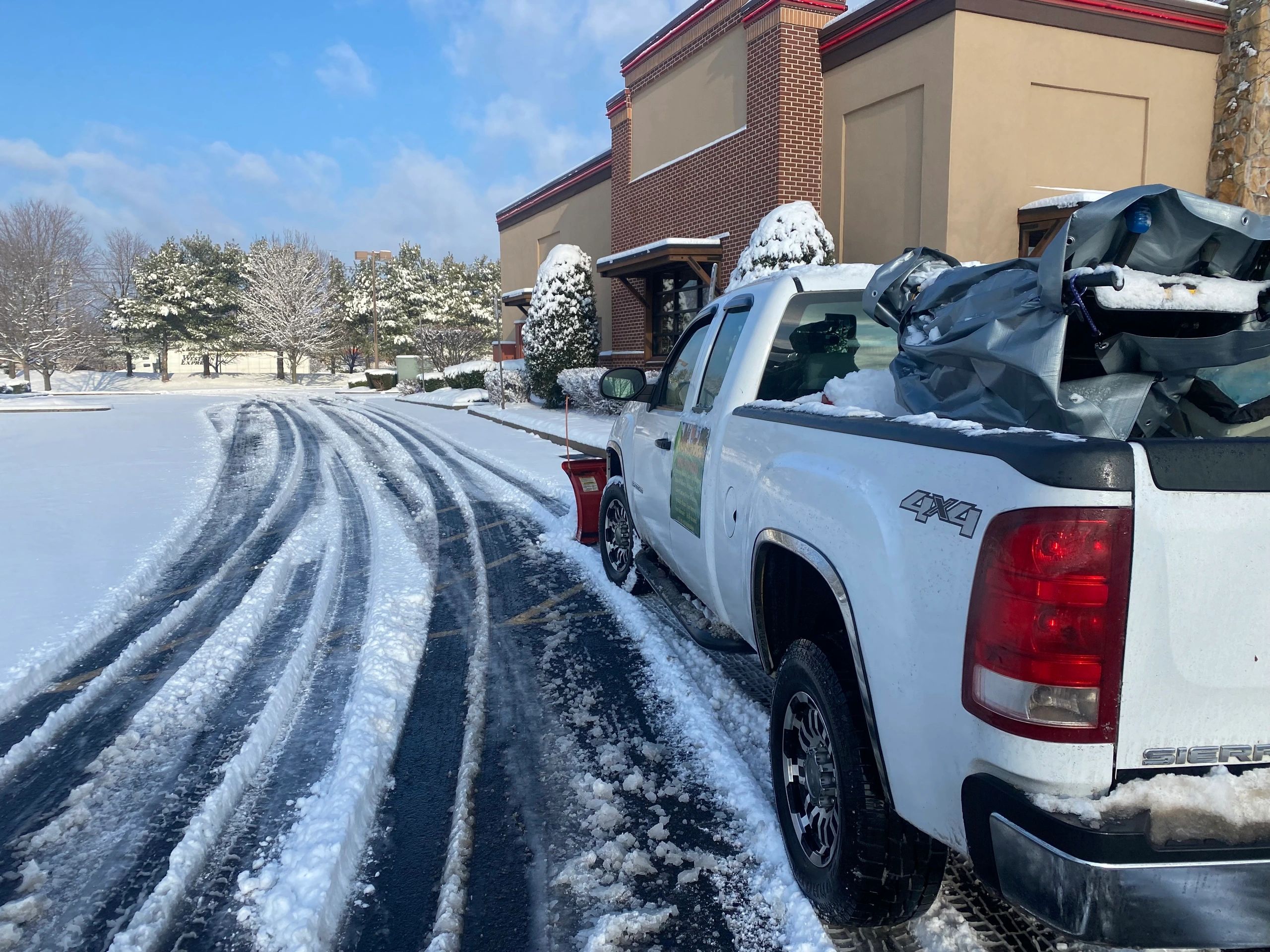 Pickup truck with snowplow clearing snow in a parking lot.