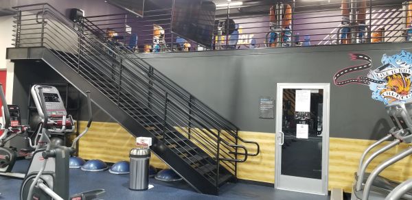 Indoor gym with stairs, exercise equipment, and mural.