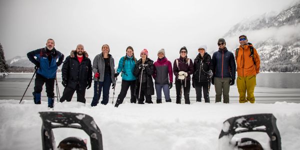 A group of young adults on a weekend retreat in winter gear standing on the edge of a lake in snow