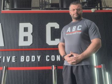 Man standing confidently in front of a fitness center sign.
