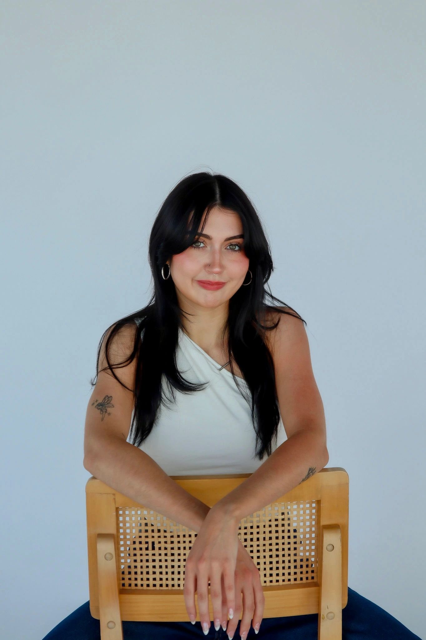 Young woman with long black hair and tattoos, smiling gently.