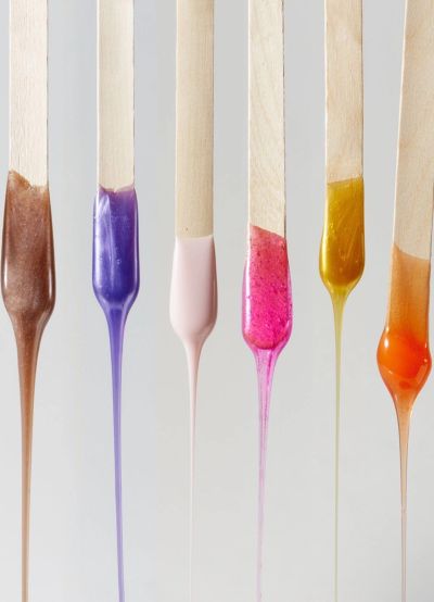 Six wooden sticks dipped in colorful, dripping nail polish in various shades.