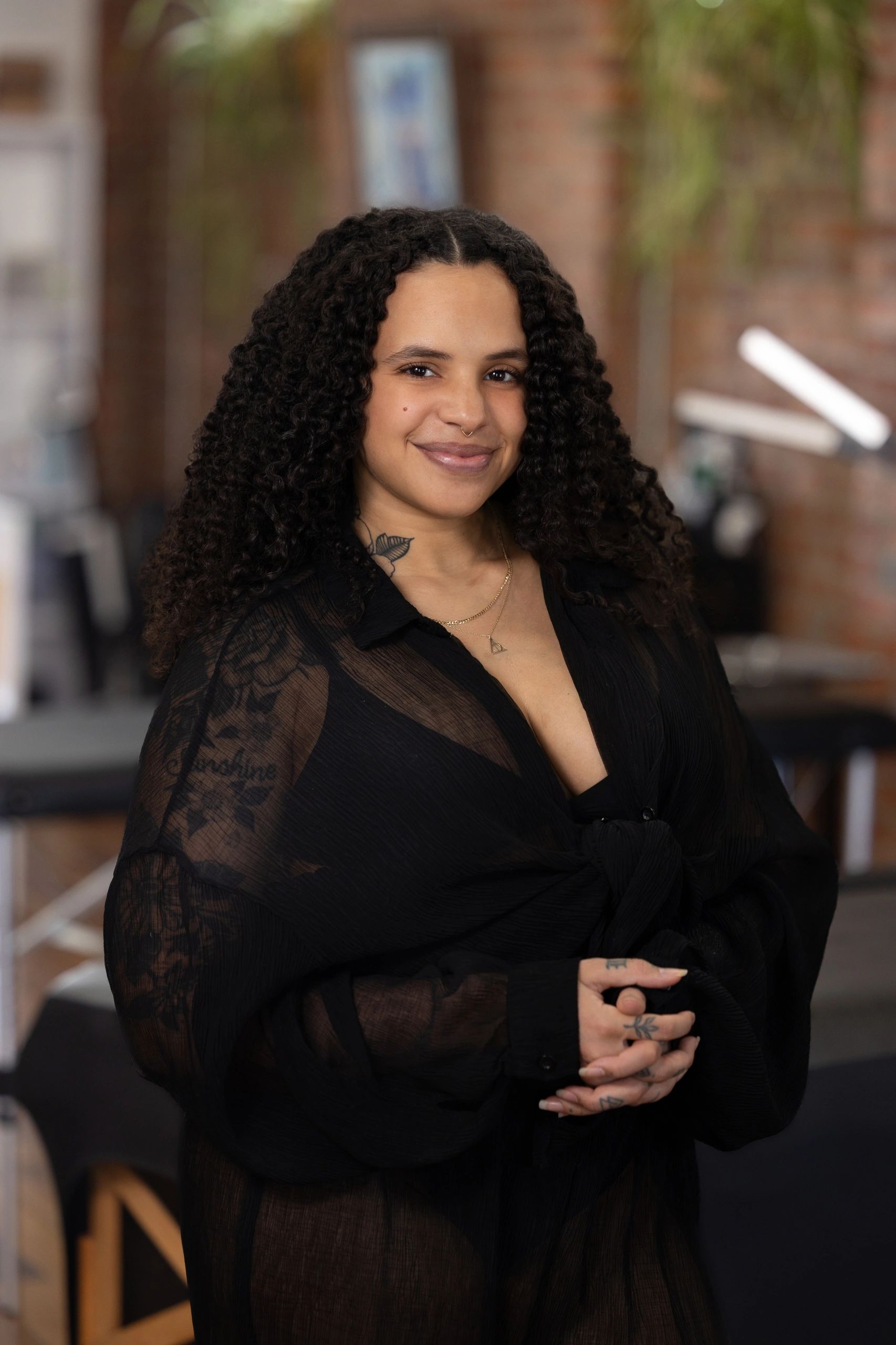 Smiling woman with curly hair wearing a black lace top and a delicate necklace.