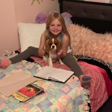 My daughter reading with a Cavalier puppy.