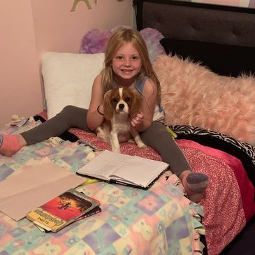 My daughter reading with a Cavalier puppy.