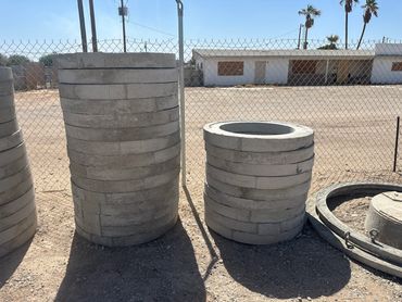 Concrete cylinders stacked outdoors near a chain-link fence.