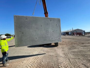 Worker overseeing large concrete slab being lifted.