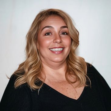Smiling woman with blonde hair in a black top against a plain background.