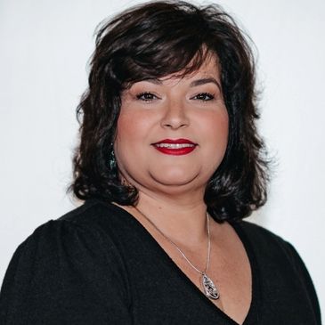 Confident woman with dark hair and red lipstick wearing a black top and silver necklace.