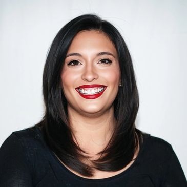 Smiling woman with dark hair and bold red lipstick against a plain background.