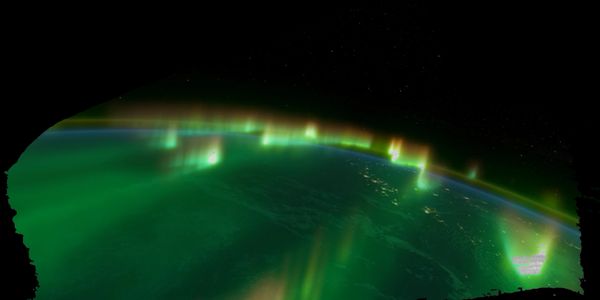 Aurora lights glow over Earth's horizon as seen from space.