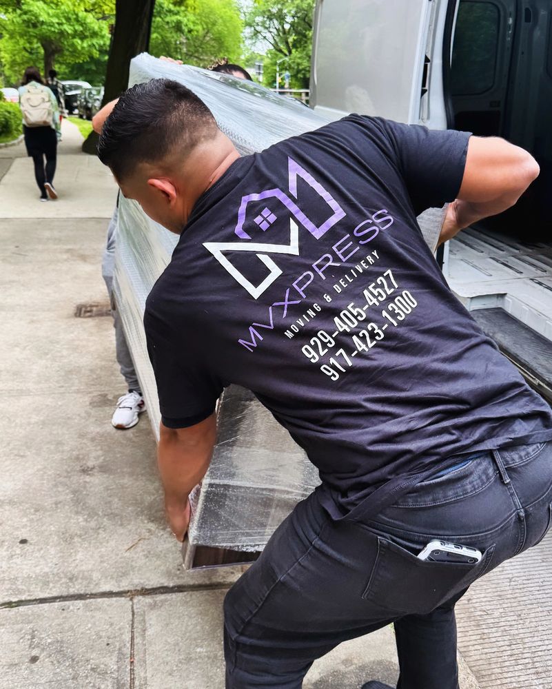 Two movers carrying a large wrapped item near a truck on a city sidewalk.