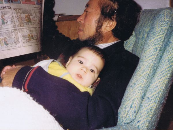 Older man holds a baby in his lap as he reads a Doonesbury comic strip in the paper