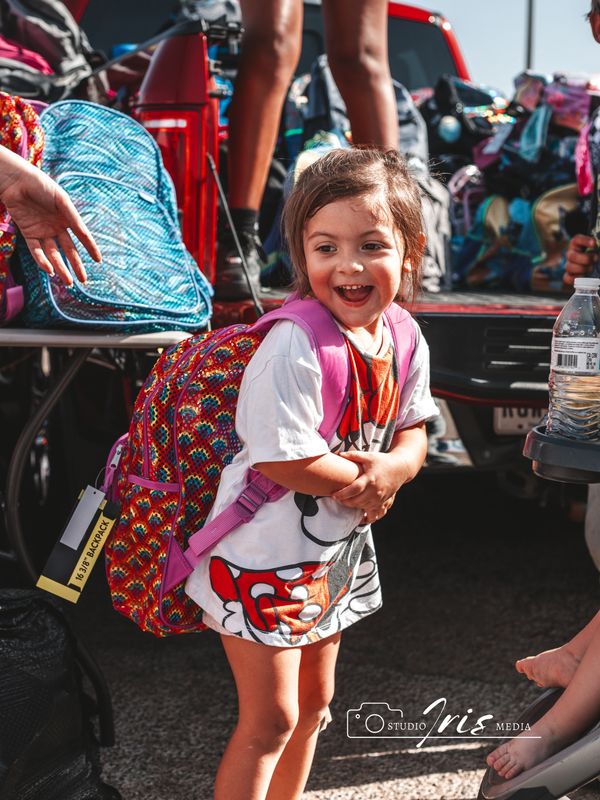 A joyful little girl wearing a colorful backpack and Mickey Mouse shirt.