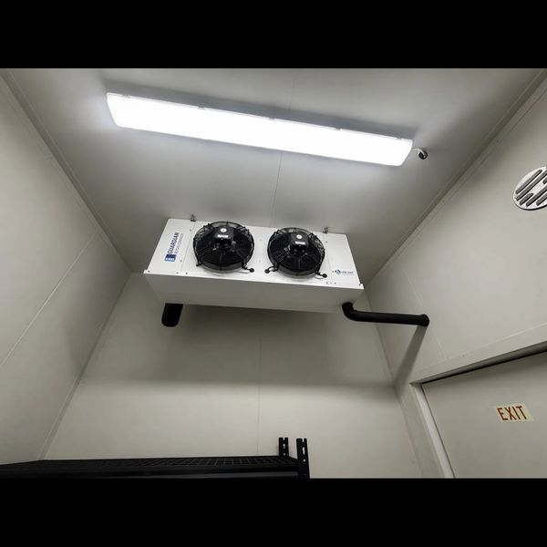 Ceiling-mounted industrial cooling unit with dual fans in a plain room.