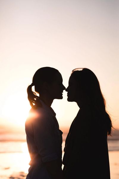 2 people holding hands, looking at each other, with the sunset in the background.