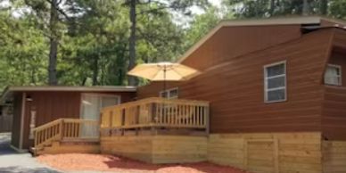 A brown wooden house with a deck and umbrella in a wooded area.