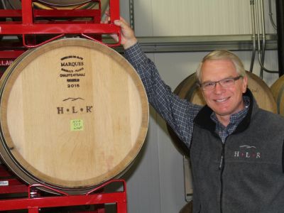 Man smiling beside a wine barrel in a cellar.